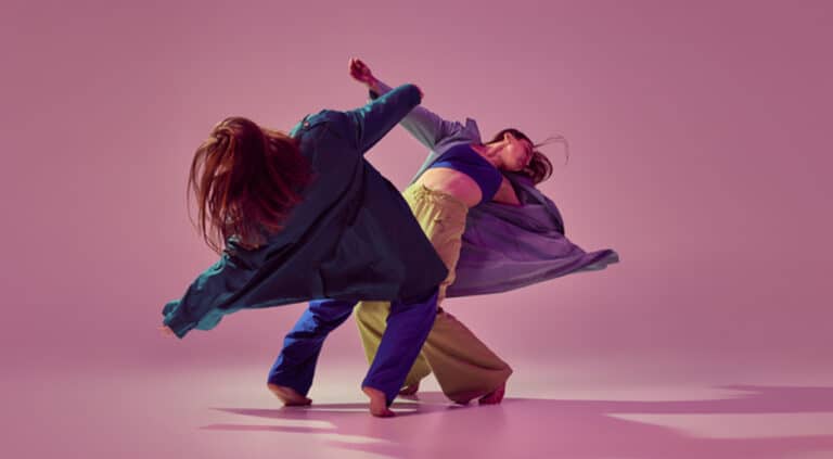Two women dancing against a pink background