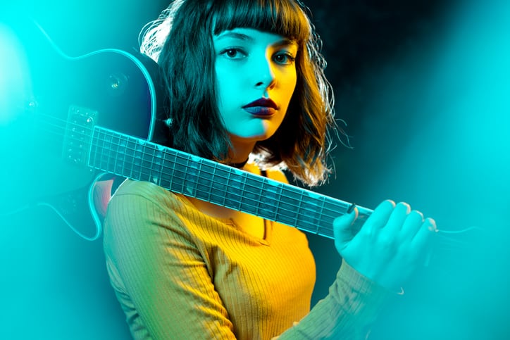 Belle jeune femme hipster aux cheveux bouclés avec une guitare rouge dans les néons. Concept de style des années 90