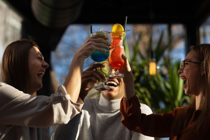 Tres amigos multirraciales en un animado bar. Fiesta afterwork con cócteles tras un exitoso día de trabajo.