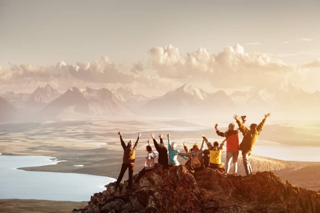 Un grand groupe de personnes s'amusant dans la pose réussie avec les bras levés au sommet de la montagne contre les lacs et les montagnes au coucher du soleil. Concept de voyage, d'aventure ou d'expédition