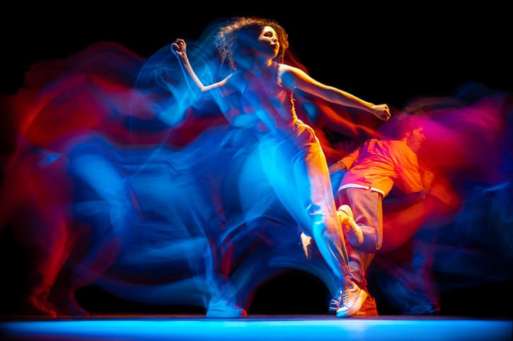 Énergie. Portrait dynamique d'un homme et d'une fille élégants dansant du hip-hop dans des vêtements de style sportif sur fond sombre à la salle de danse en néon mixte. Culture jeunesse, hip-hop, mouvement, style et mode, action.