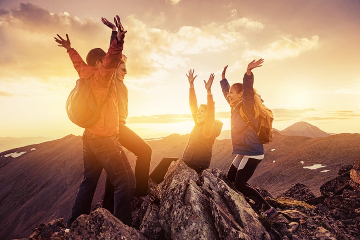 Quatre collègues de travail heureux célébrant l'escalade au sommet de la montagne au coucher du soleil