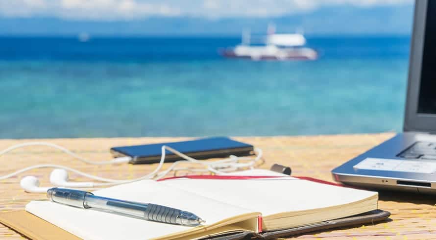 Livre posé sur une table sur la plage avec un ordinateur et un stylo
