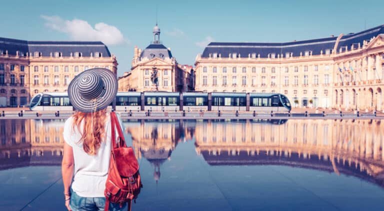 Rear view of a woman arriving at Place de la Bourse for a company party. Buildings reflecting the water mirror in Bordeaux