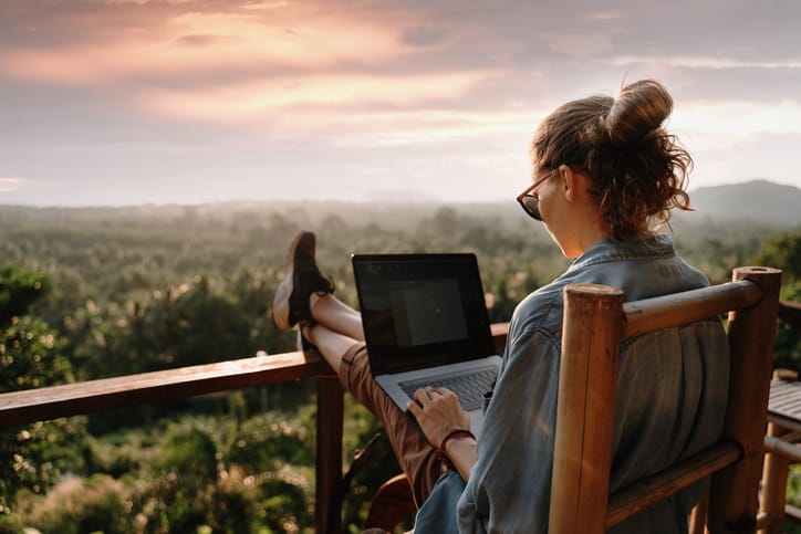 Jeune femme d'affaires travaillant à l'ordinateur au café sur le rocher. Rétrogradation de jeune fille travaillant sur un ordinateur portable au coucher ou au lever du soleil au sommet de la montagne jusqu'à la mer, journée de travail.