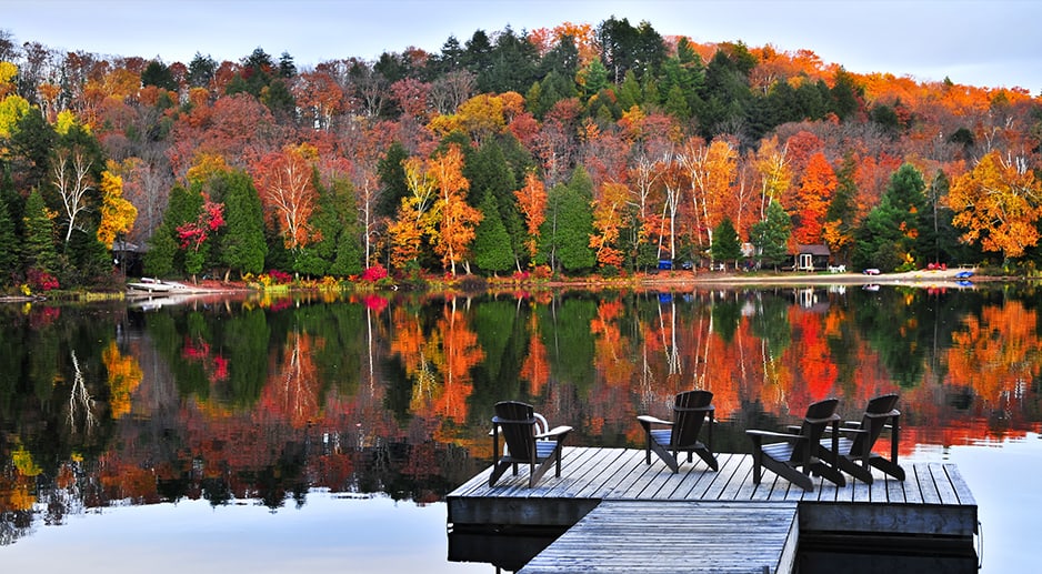 Un lac une journée d'automne avec un ponton et des chaises. Les arbres sont de couleurs verts, oranges, jaunes