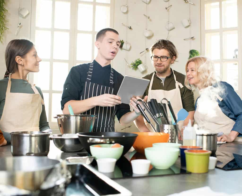 Group of young and mature people in aprons taking a cooking class.
