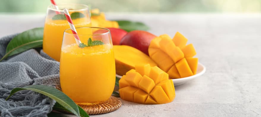 Smoothie frais délicieux de jus de mangue dans une cave de verre sur le fond gris de table