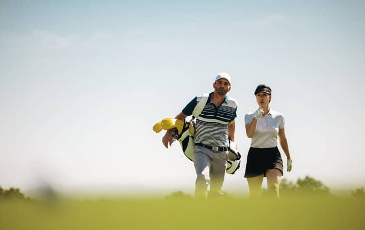 Une sportive et son instructeur de golf s'engagent dans la planification d'une stratégie lors d'un match de golf, en se concentrant sur le travail d'équipe et la compétition sous un ciel clair.