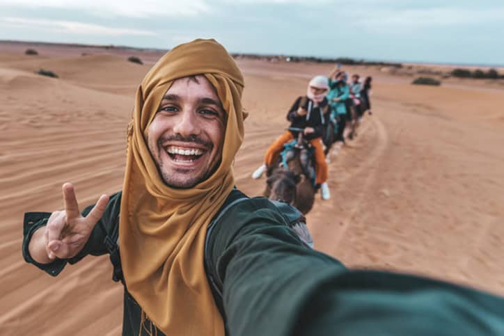 Empleados felices disfrutando de un paseo en camello por el desierto en grupo.